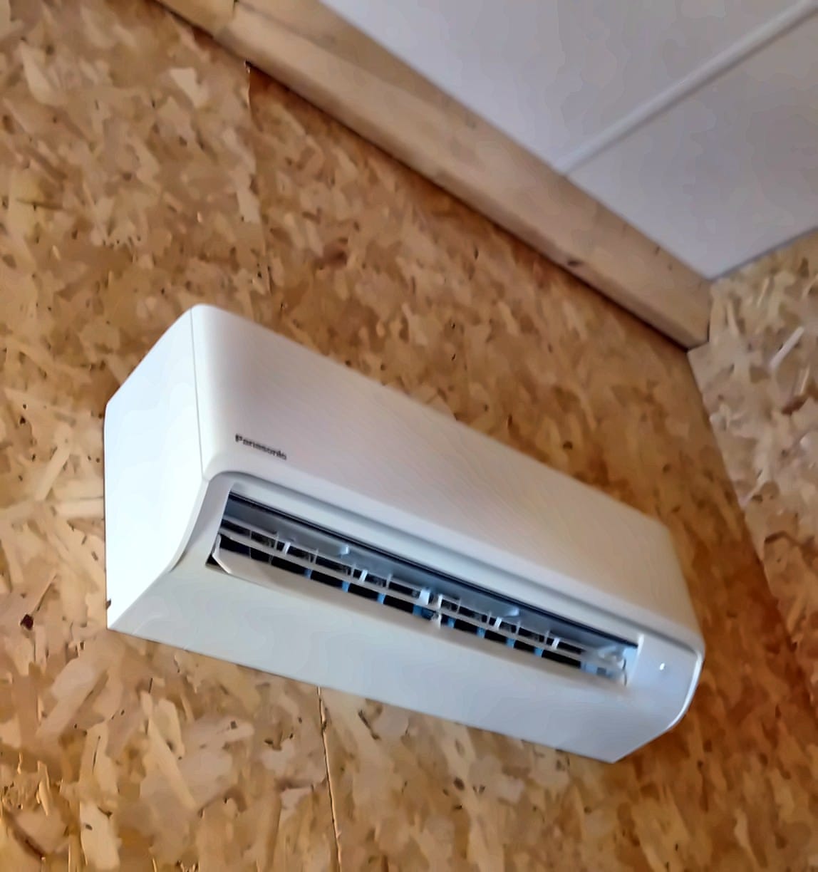 Witte binnenunit van een airco aan een wand van OSB-platen