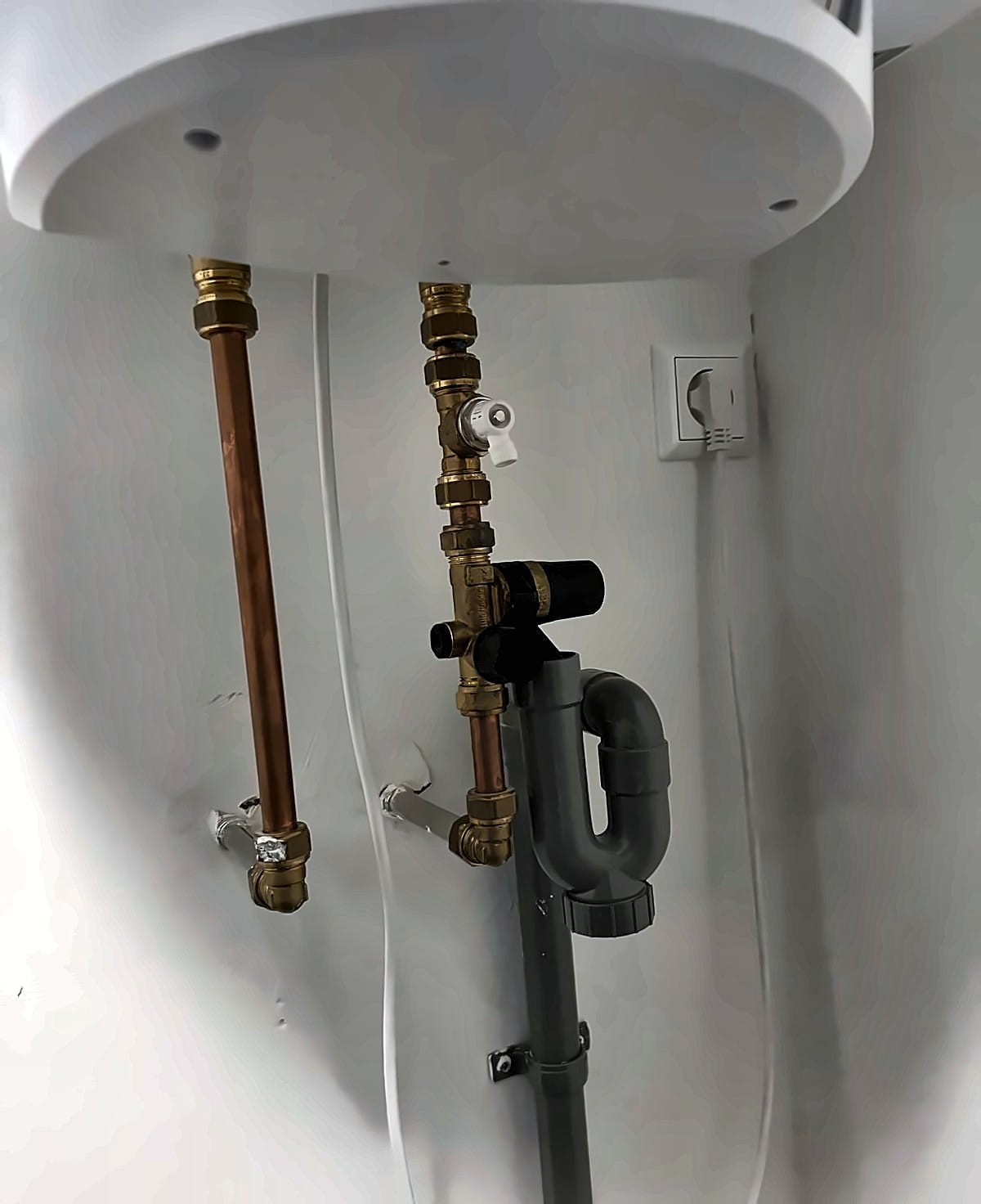 Onderkant van een elektrische boiler met koperen leidingen, inlaatcombinatie en sifon